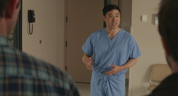 Movie still from “The Hollars” (2016), directed by John Krasinski – A man in blue scrubs talking to a man in a blue shirt; Medium shot, Over the shoulder angle