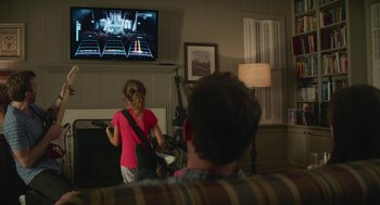 Movie still from “The Hollars” (2016), directed by John Krasinski – Two people playing a video game in a living room; Medium shot, Over the shoulder angle