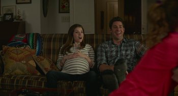 Movie still from “The Hollars” (2016), directed by John Krasinski – A man and a pregnant woman sitting on a couch; Medium shot, Over the shoulder angle