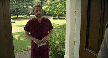 Movie still from “The Hollars” (2016), directed by John Krasinski – A man standing in front of a porch holding a paper; Medium shot, Over the shoulder angle