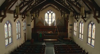 Movie still from “The Hollars” (2016), directed by John Krasinski – An organ in a church with a man sitting in a pew; Extreme Wide shot, Low angle