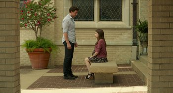 Movie still from “The Hollars” (2016), directed by John Krasinski – A man and a woman sitting on top of a stone bench; Wide shot, High angle