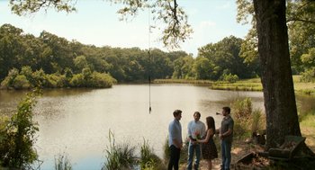 Movie still from “The Hollars” (2016), directed by John Krasinski – A group of people standing next to a body of water; Extreme Wide shot, High angle
