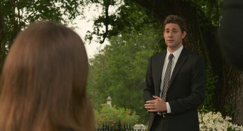 Movie still from “The Hollars” (2016), directed by John Krasinski – A man in a suit and tie talking to a woman in a suit; Medium shot, Over the shoulder angle