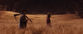 Movie still from “The Host” (2013), directed by Andrew Niccol – A man and a woman are in a field with a gun; Wide shot, Over the shoulder angle