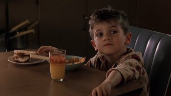 Movie still from “The Hours” (2002), directed by Stephen Daldry – A boy sitting at a table with a bowl of cereal and a glass of orange juice in front of him; Close Up shot, High angle