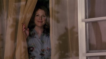 Movie still from “The Hours” (2002), directed by Stephen Daldry – A woman standing in front of a window with curtains; Medium shot, Over the shoulder angle