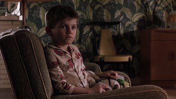 Movie still from “The Hours” (2002), directed by Stephen Daldry – A young boy sitting in a chair holding a remote control; Medium shot, High angle