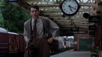 Movie still from “The Hours” (2002), directed by Stephen Daldry – A man standing in front of a train station with his hands in his pockets; Medium shot, Low angle