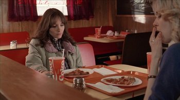 Movie still from “The House of the Devil” (2009), directed by Ti West – A woman sitting at a table in a restaurant eating pizza; Medium shot, High angle