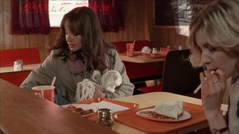 Movie still from “The House of the Devil” (2009), directed by Ti West – A woman sitting at a table in front of a plate of food; Medium shot, Over the shoulder angle