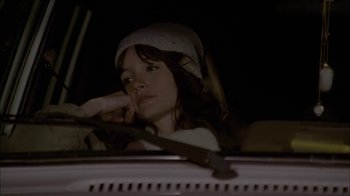 Movie still from “The House of the Devil” (2009), directed by Ti West – A woman sitting in the driver's seat of a car at night; Close Up shot, Over the shoulder angle