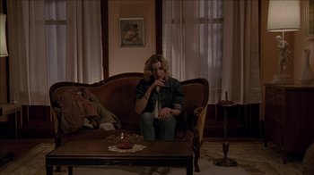 Movie still from “The House of the Devil” (2009), directed by Ti West – A woman sitting on a couch in a living room; Wide shot, High angle