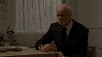 Movie still from “The House of the Devil” (2009), directed by Ti West – An older man wearing a suit and tie holding a pair of scissors; Medium shot, Over the shoulder angle