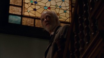 Movie still from “The House of the Devil” (2009), directed by Ti West – An older man standing in front of a stained glass window; Medium shot, Low angle