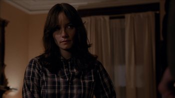 Movie still from “The House of the Devil” (2009), directed by Ti West – A woman in a plaid shirt standing in front of a window; Close Up shot, Over the shoulder angle