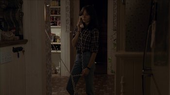 Movie still from “The House of the Devil” (2009), directed by Ti West – A woman talking on a phone while standing in a room; Medium shot, High angle
