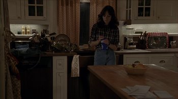 Movie still from “The House of the Devil” (2009), directed by Ti West – A woman standing in a kitchen holding a coffee mug; Medium shot, High angle
