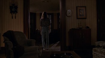 Movie still from “The House of the Devil” (2009), directed by Ti West – A woman standing in a living room in front of an open door; Wide shot, High angle