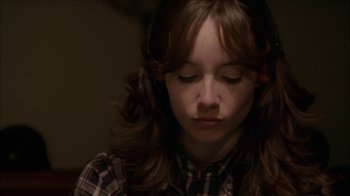 Movie still from “The House of the Devil” (2009), directed by Ti West – A young girl with long brown hair wearing headphones; Close Up shot, Over the shoulder angle