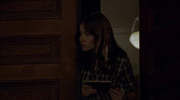 Movie still from “The House of the Devil” (2009), directed by Ti West – A woman standing in a doorway holding a book; Medium shot, Over the shoulder angle