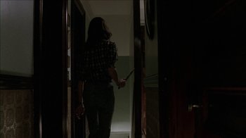 Movie still from “The House of the Devil” (2009), directed by Ti West – A woman holding a knife in a dark room; Medium shot, Low angle
