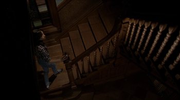 Movie still from “The House of the Devil” (2009), directed by Ti West – A man standing on the bottom of a wooden staircase; Wide shot, Overhead angle