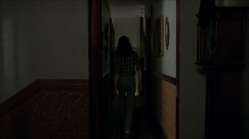Movie still from “The House of the Devil” (2009), directed by Ti West – A woman walking down a hallway in the dark; Wide shot, Over the shoulder angle