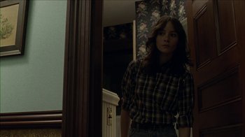 Movie still from “The House of the Devil” (2009), directed by Ti West – A woman standing in front of a mirror in a room; Medium shot, Over the shoulder angle