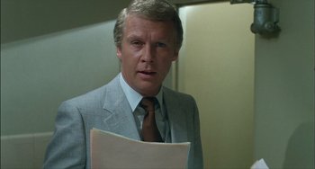 Movie still from “The Howling” (1981), directed by Joe Dante – A person wearing a suit and tie holding papers; Close Up shot, Over the shoulder angle