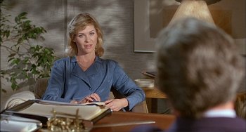 Movie still from “The Howling” (1981), directed by Joe Dante – A woman sitting at a table in front of a book; Medium shot, Over the shoulder angle