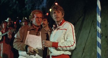 Movie still from “The Howling” (1981), directed by Joe Dante – Two men standing next to each other in front of lights; Medium shot, Over the shoulder angle