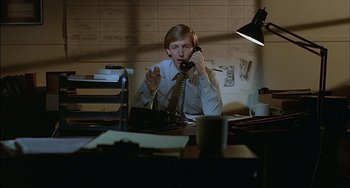 Movie still from “The Howling” (1981), directed by Joe Dante – A man sitting at a desk talking on a phone; Medium shot, High angle