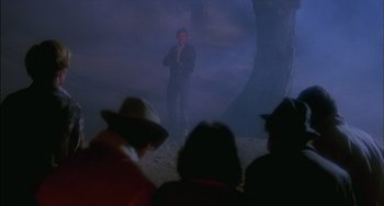 Movie still from “The Howling” (1981), directed by Joe Dante – A man standing in front of a group of people; Wide shot, Over the shoulder angle