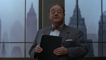 Movie still from “The Hudsucker Proxy” (1994), directed by Ethan Coen – A man in a suit and bow tie holding a black folder; Medium shot, Low angle