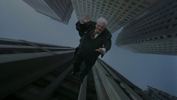 Movie still from “The Hudsucker Proxy” (1994), directed by Ethan Coen – An old man in a suit and tie is jumping off a flight of stairs in a city; Wide shot, Overhead angle
