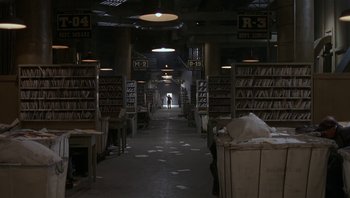 Movie still from “The Hudsucker Proxy” (1994), directed by Ethan Coen – A person is walking through an aisle in a library; Extreme Wide shot, High angle