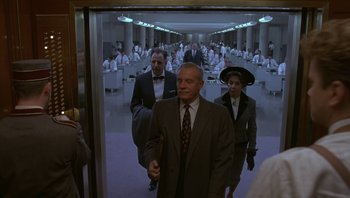 Movie still from “The Hudsucker Proxy” (1994), directed by Ethan Coen – A group of people in suits walking in a room; Wide shot, Low angle