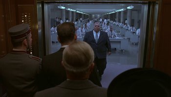 Movie still from “The Hudsucker Proxy” (1994), directed by Ethan Coen – A man in a suit walks through a room full of people; Wide shot, Low angle