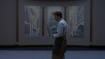 Movie still from “The Hudsucker Proxy” (1994), directed by Ethan Coen – A man standing in front of a wall with paintings on it; Wide shot, Low angle