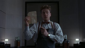 Movie still from “The Hudsucker Proxy” (1994), directed by Ethan Coen – A man holding a piece of paper and pointing to it; Medium shot, Low angle