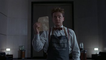Movie still from “The Hudsucker Proxy” (1994), directed by Ethan Coen – A man holding a piece of paper in his hand; Medium shot, Low angle