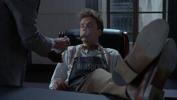 Movie still from “The Hudsucker Proxy” (1994), directed by Ethan Coen – A man sitting in an office chair with a cigar in his mouth; Medium shot, High angle