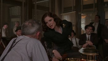 Movie still from “The Hudsucker Proxy” (1994), directed by Ethan Coen – A woman in a black jacket is holding a knife in her hand; Medium shot, Over the shoulder angle