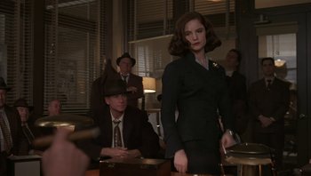 Movie still from “The Hudsucker Proxy” (1994), directed by Ethan Coen – A man and a woman in a suit and tie in a room; Medium shot, Over the shoulder angle