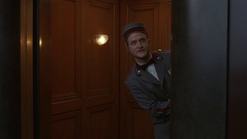 Movie still from “The Hudsucker Proxy” (1994), directed by Ethan Coen – A man in a uniform standing next to a pillar; Medium shot, Low angle