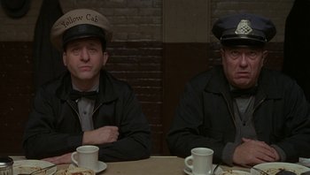 Movie still from “The Hudsucker Proxy” (1994), directed by Ethan Coen – Two men sitting at a table with coffee cups; Medium shot, Low angle