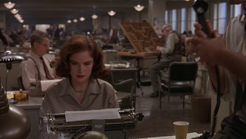 Movie still from “The Hudsucker Proxy” (1994), directed by Ethan Coen – A woman sitting at a typewriter in a room filled with people; Medium shot, Low angle