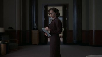 Movie still from “The Hudsucker Proxy” (1994), directed by Ethan Coen – A woman standing in front of an open door holding a tablet; Medium shot, Low angle
