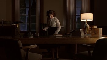 Movie still from “The Hudsucker Proxy” (1994), directed by Ethan Coen – A woman standing at a table in front of a window; Wide shot, Low angle